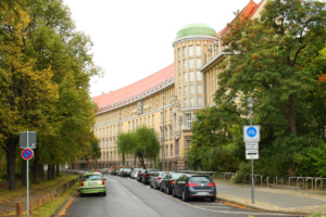 Straße mit großem Gebäude und parkenden Autos.