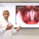Prof. Michael Fuchs demonstriert die Funktion der Stimmlippen beim Singen vor einem Bild.